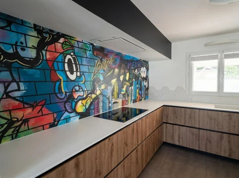 Professionnel dans un t-shirt ou vêtement de travail debout sur un chantier de rénovation intérieure, tenant un plan ou tablette numérique, supervisé par plusieurs ouvriers en arrière-plan travaillant sur différentes tâches (un peintre avec ses équipements de peinture, quelqu'un posant du carrelage ou un revêtement, quelqu'un travaillant la plâtrerie). La scène se déroule dans un intérieur résidentiel en cours de rénovation, avec des matériaux de chantier visibles. L'atmosphère doit être professionnelle et coordonnée, montrant la gestion d'un projet intégré.